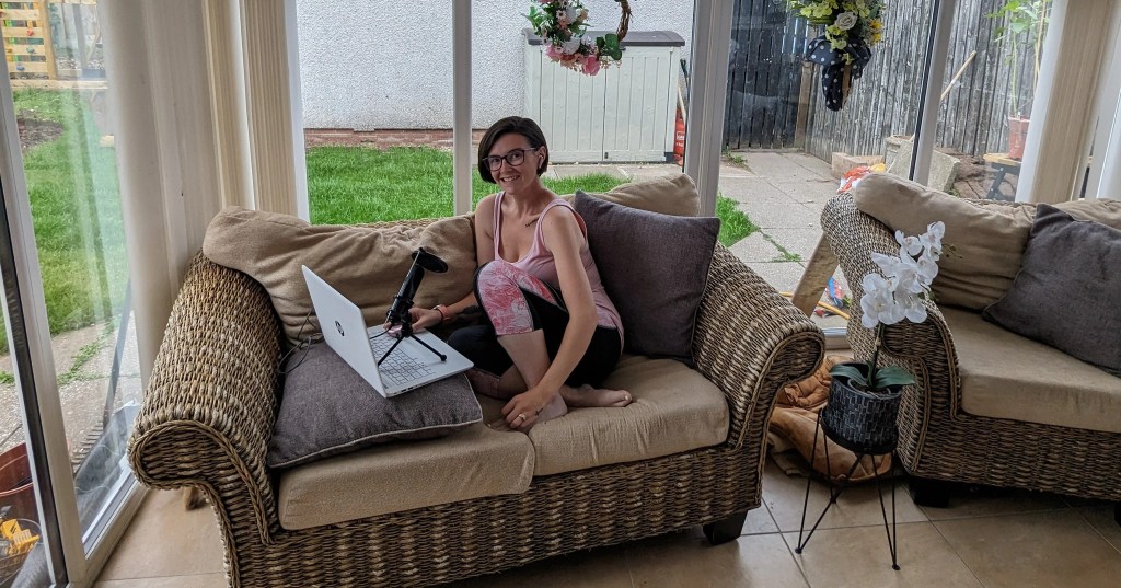 Young woman sits on conservatory sofa with a laptop and microphone